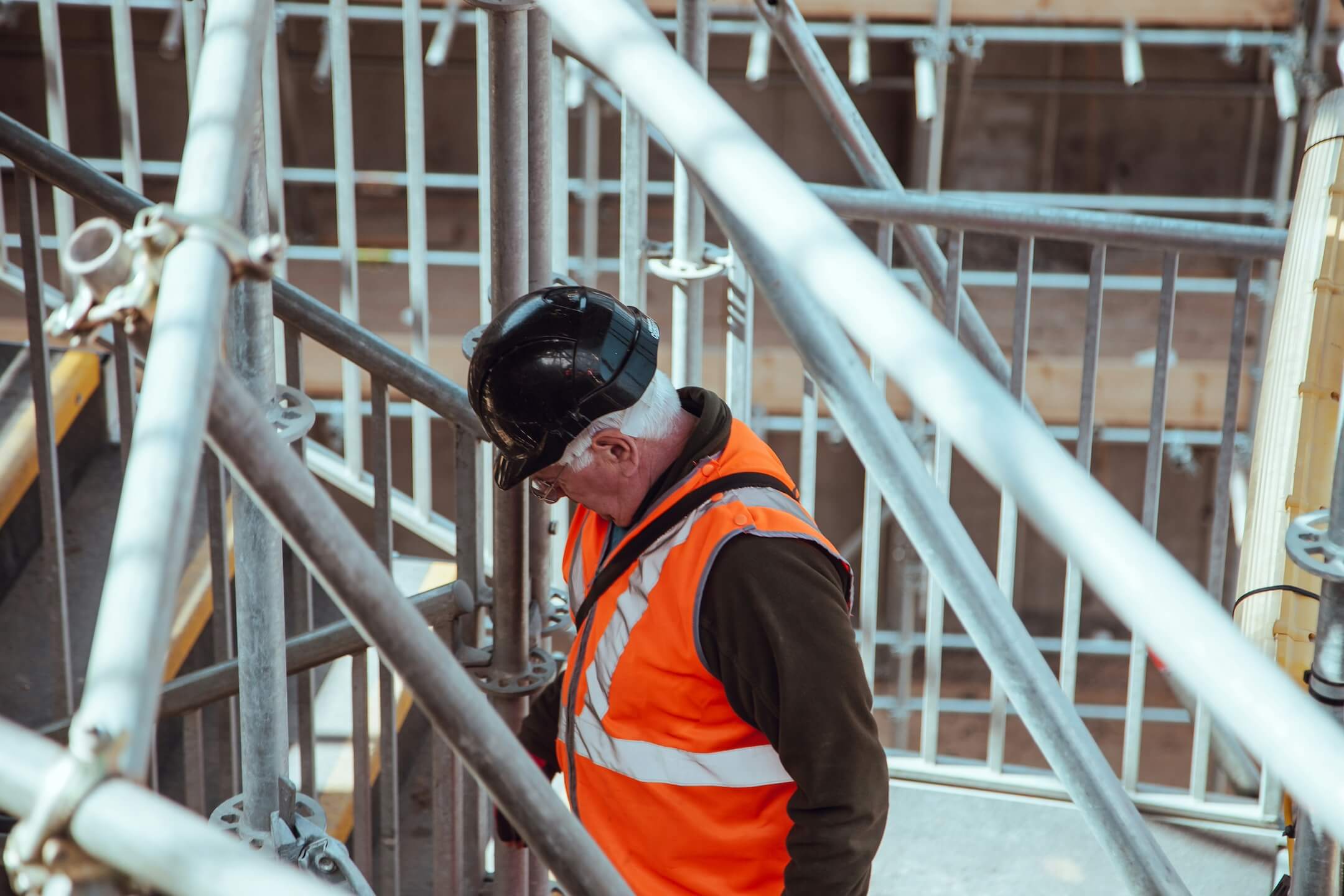 Arbeiter in Sicherheitsausrüstung überprüft Gerüstbau auf einer Baustelle, repräsentiert die Fachkompetenz, die Flexa Personal vermittelt.